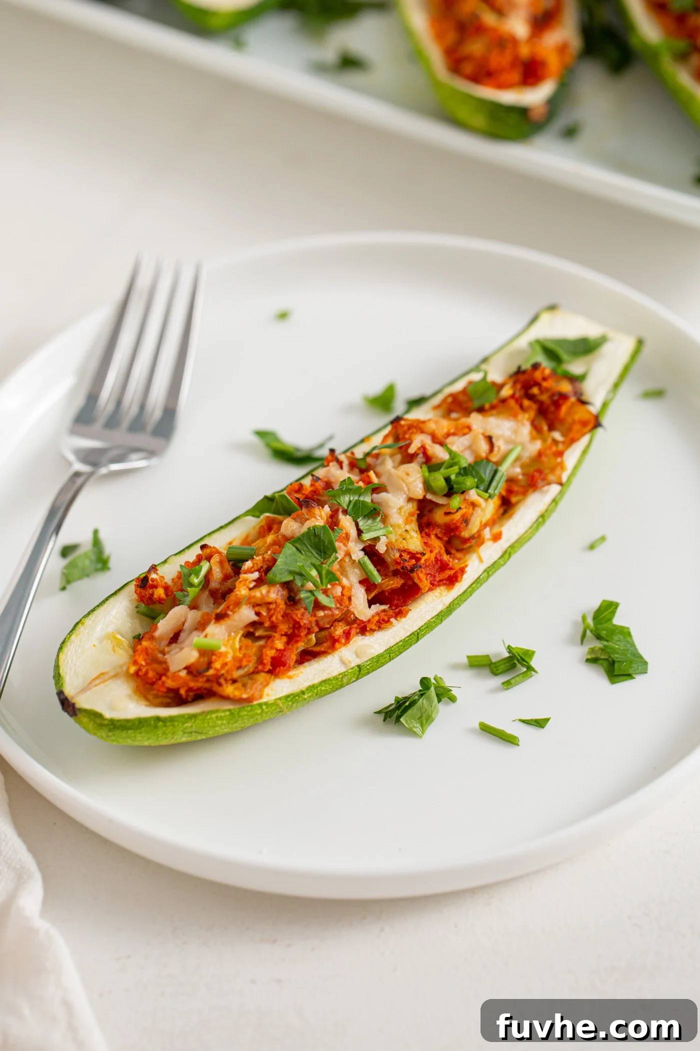 Half a zucchini on a plate stuffed with an artichoke and marinara sauce mixture. Fork rests on plate, highlighting the delicious filling.