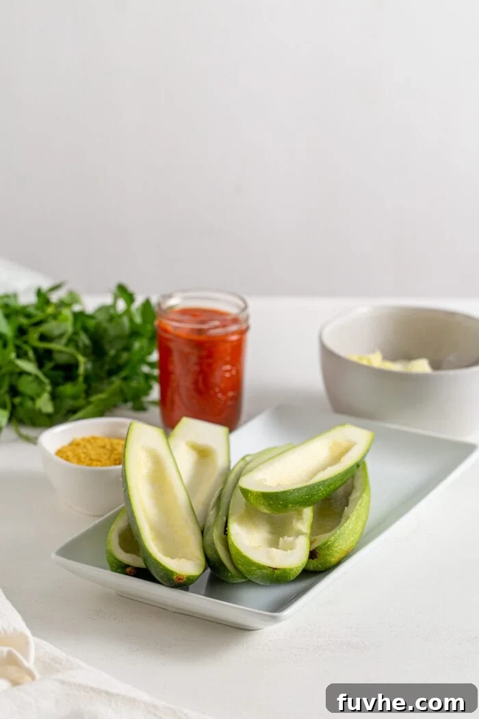 Zucchinis cut in half lengthwise with the flesh scooped out to create shells on a baking sheet.