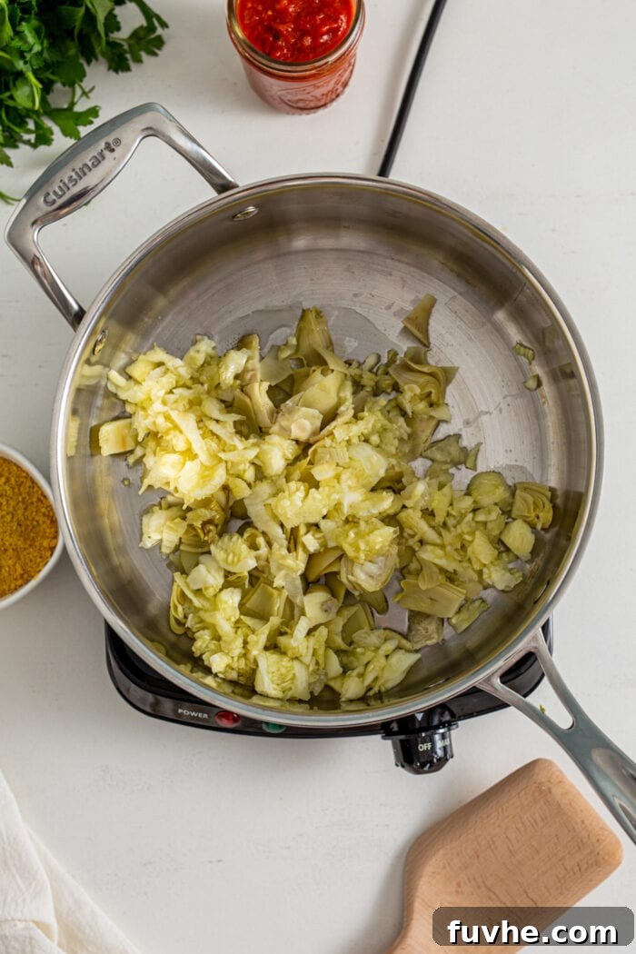 Overhead view of cooked zucchini, artichokes, and garlic simmering in a hot skillet, becoming fragrant.