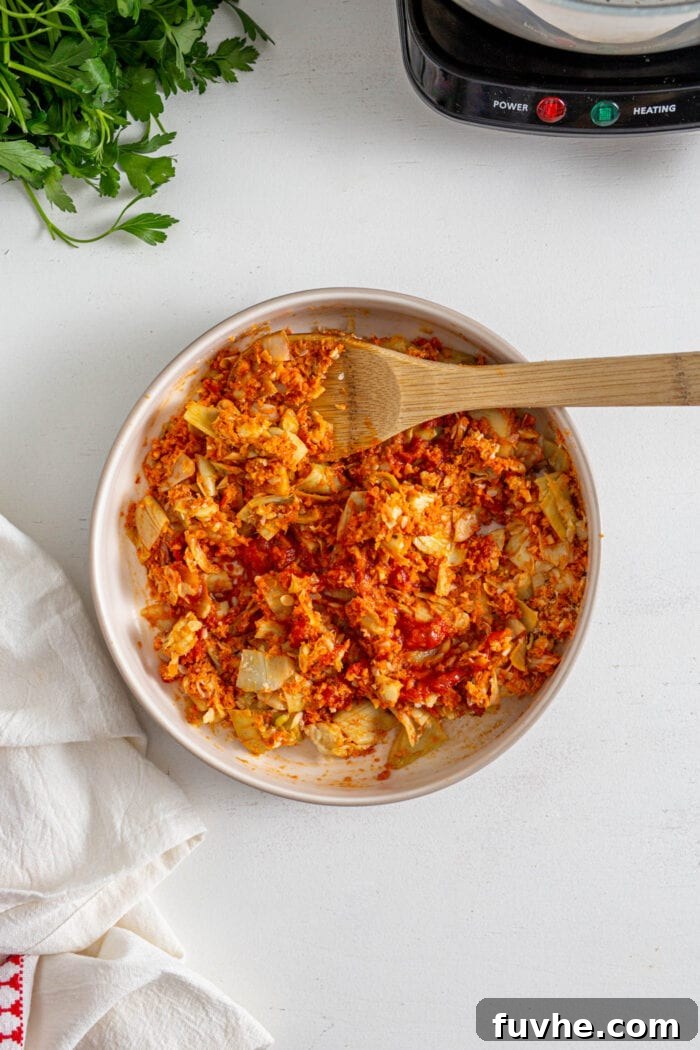 Chopped artichokes, garlic, and zucchini mixed with marinara sauce, breadcrumbs, and nutritional yeast in a bowl. A wooden spoon rests in the bowl.
