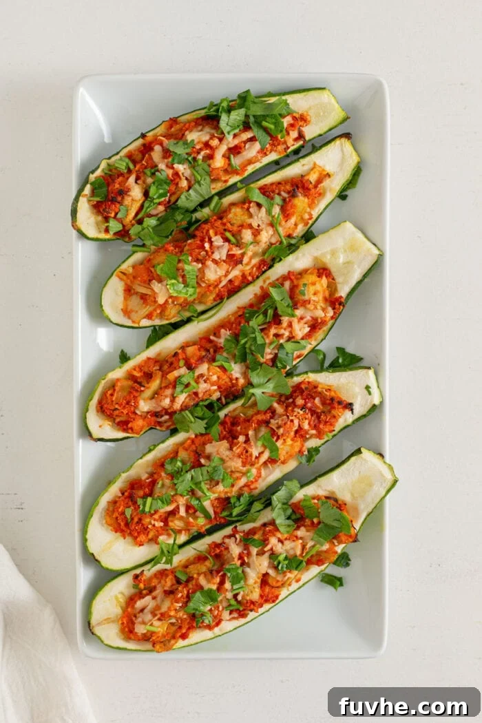 Five beautifully stuffed zucchini boats topped with fresh herbs, arranged on a rectangular plate, ready for serving.
