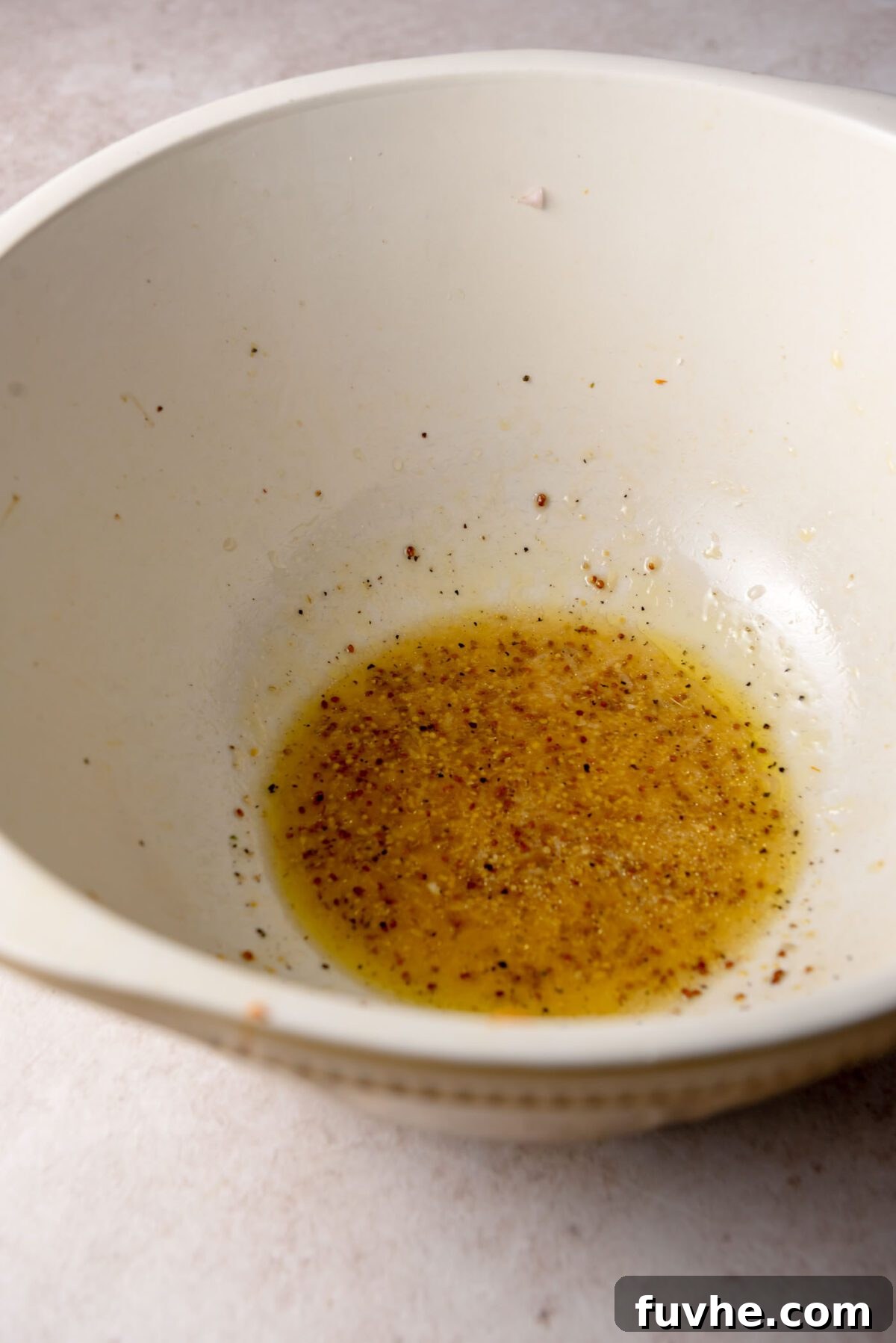 Apple cider vinaigrette with olive oil, Dijon mustard, maple syrup and spices whisked together in a white bowl.
