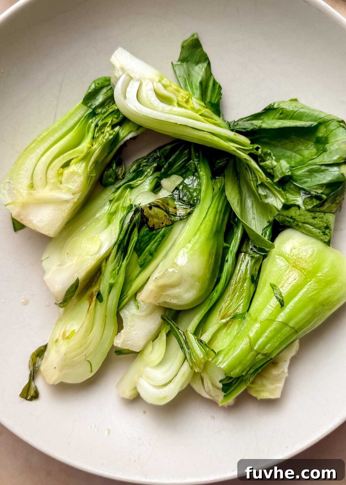 Umami Tofu Soba Bowl 5 Steamed bok choy with pale green stems and dark green leaves resting on a white plate, showing perfectly wilted leaves and tender stems.