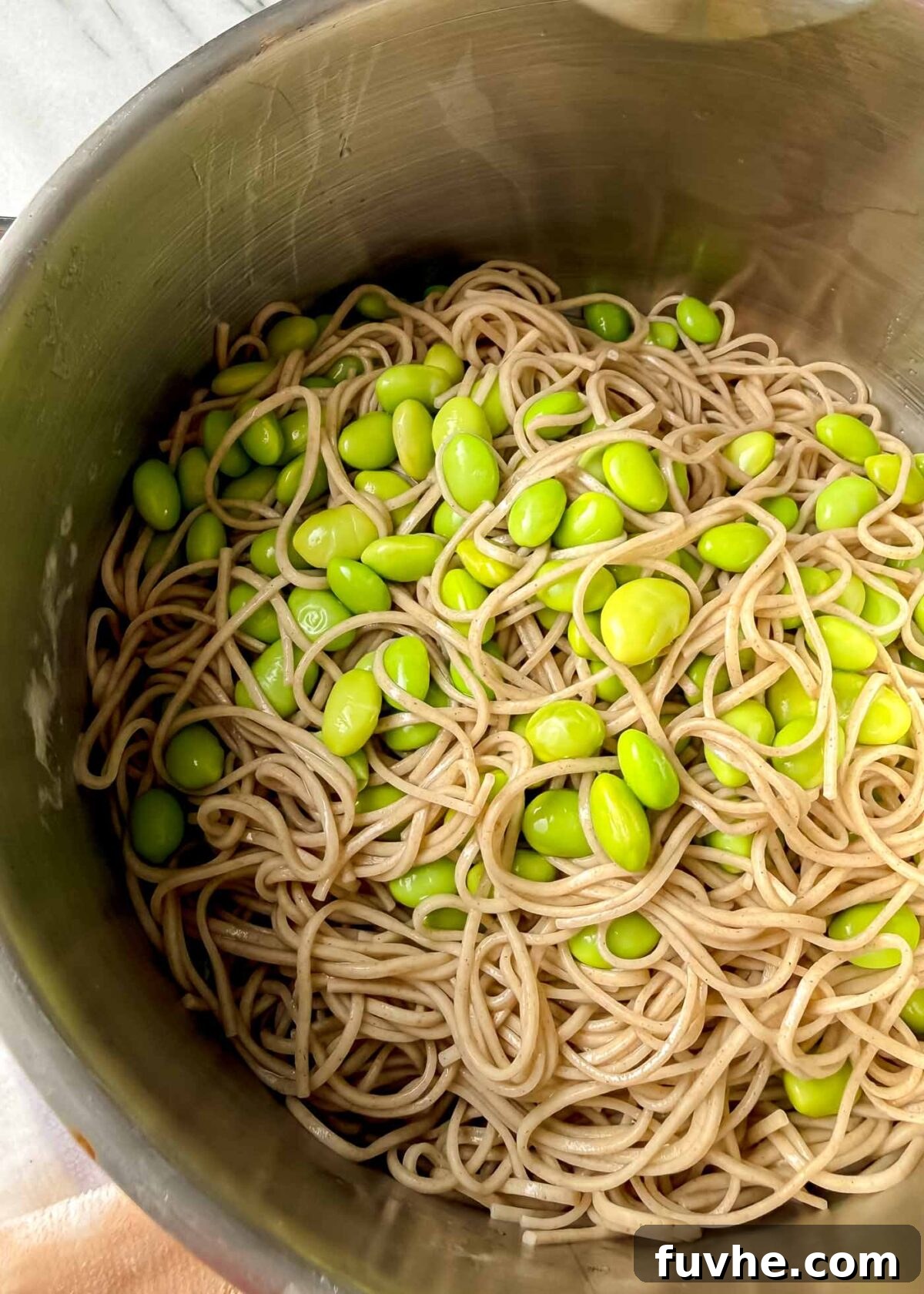 Umami Tofu Soba Bowl 7 A stainless steel pot filled with perfectly cooked soba noodles tangled together with bright green edamame beans, viewed from above to highlight the glossy noodles and vibrant beans.