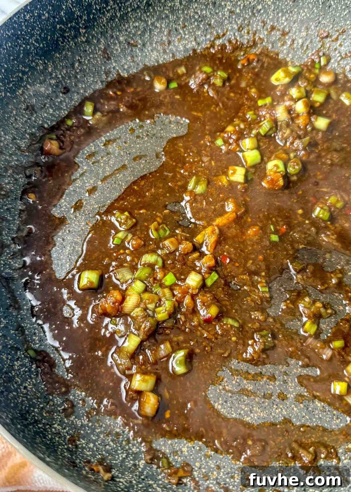 Umami Tofu Soba Bowl 8 Dark glossy sesame-soy sauce simmering in a pan, infused with chopped green onions, minced garlic, grated ginger, and small red chili flakes, creating an aromatic base.
