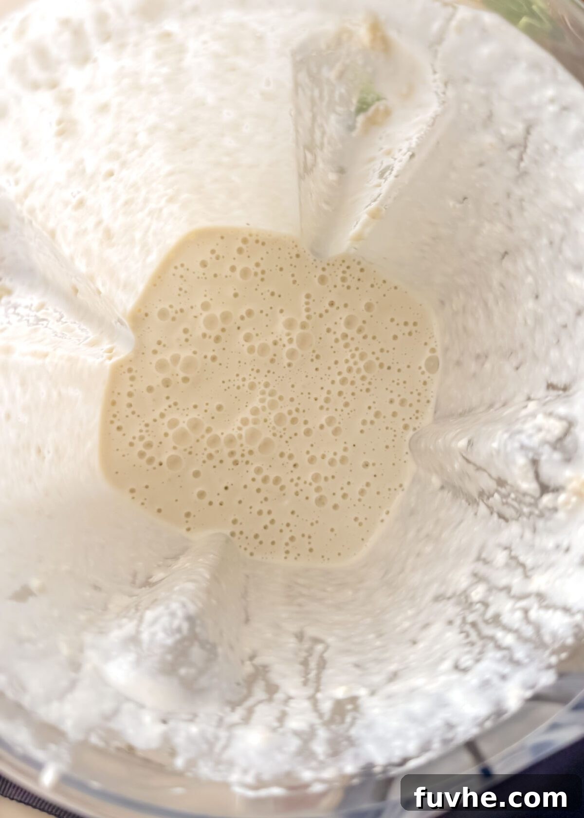 Head Over Heels for Chickpeas 4 Top-down view inside a blender containing a smooth, pale cashew cream with small air bubbles after blending soaked cashews and broth.