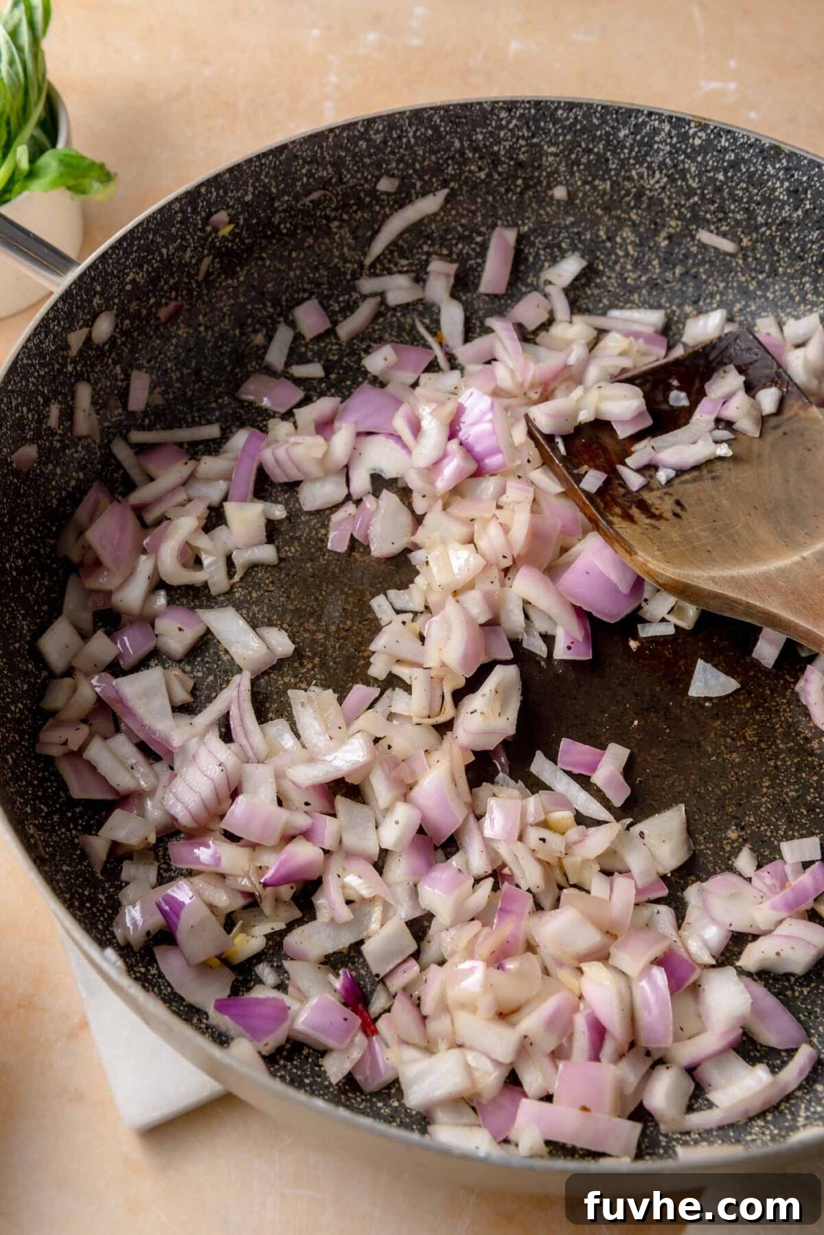 Head Over Heels for Chickpeas 5 Diced red onion sautéing in olive oil in a large nonstick skillet, with pieces beginning to soften and turn translucent as they are stirred with a wooden spoon.