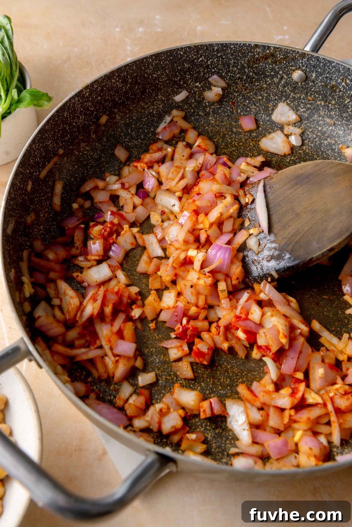 Head Over Heels for Chickpeas 6 Softened red onion cooking in a skillet with minced garlic, red chili flakes, and tomato paste, creating a deep red, fragrant base for the sauce.