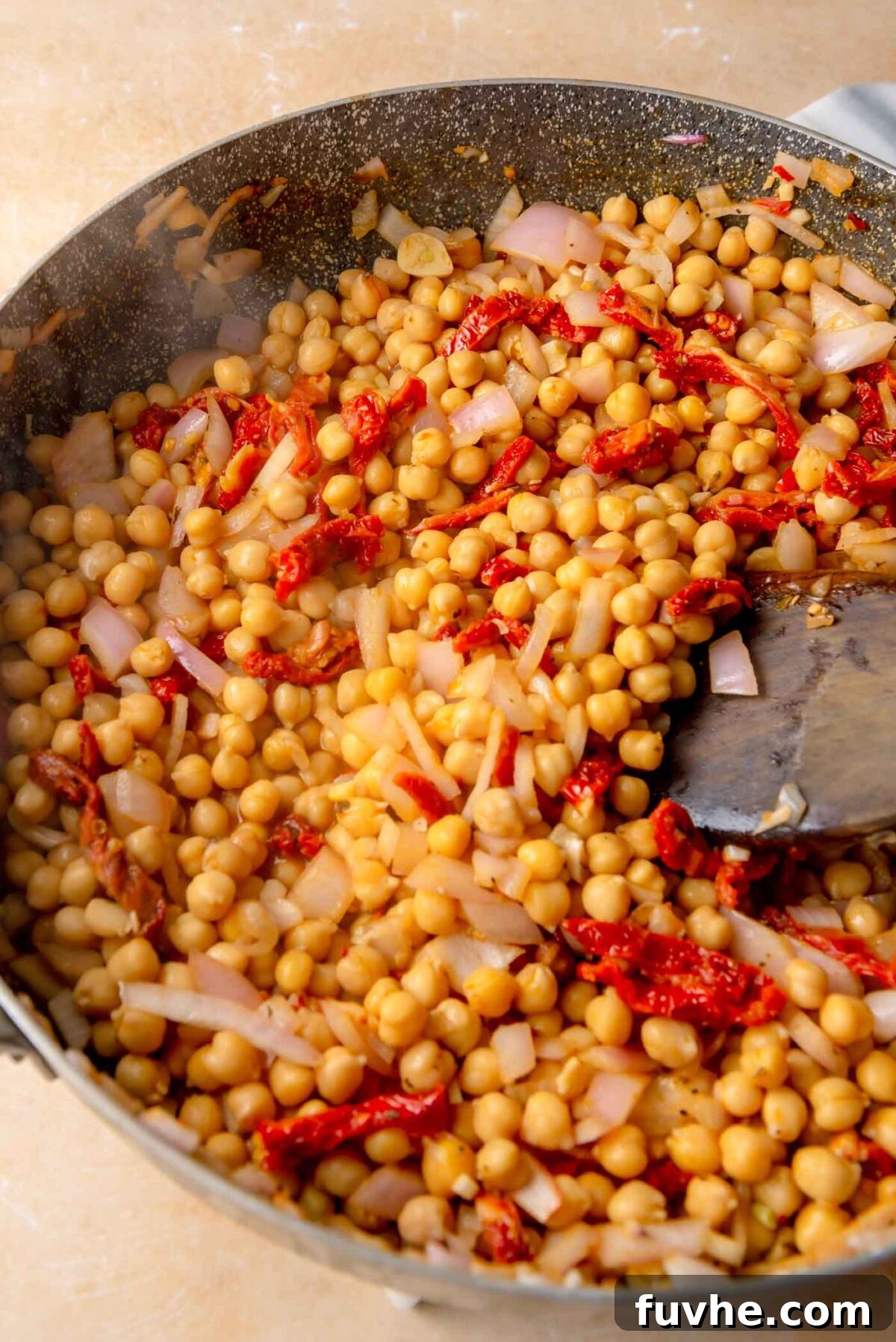 Head Over Heels for Chickpeas 7 Cooked chickpeas and sliced sun-dried tomatoes in a skillet with an onion mixture, being stirred together as the flavors combine.