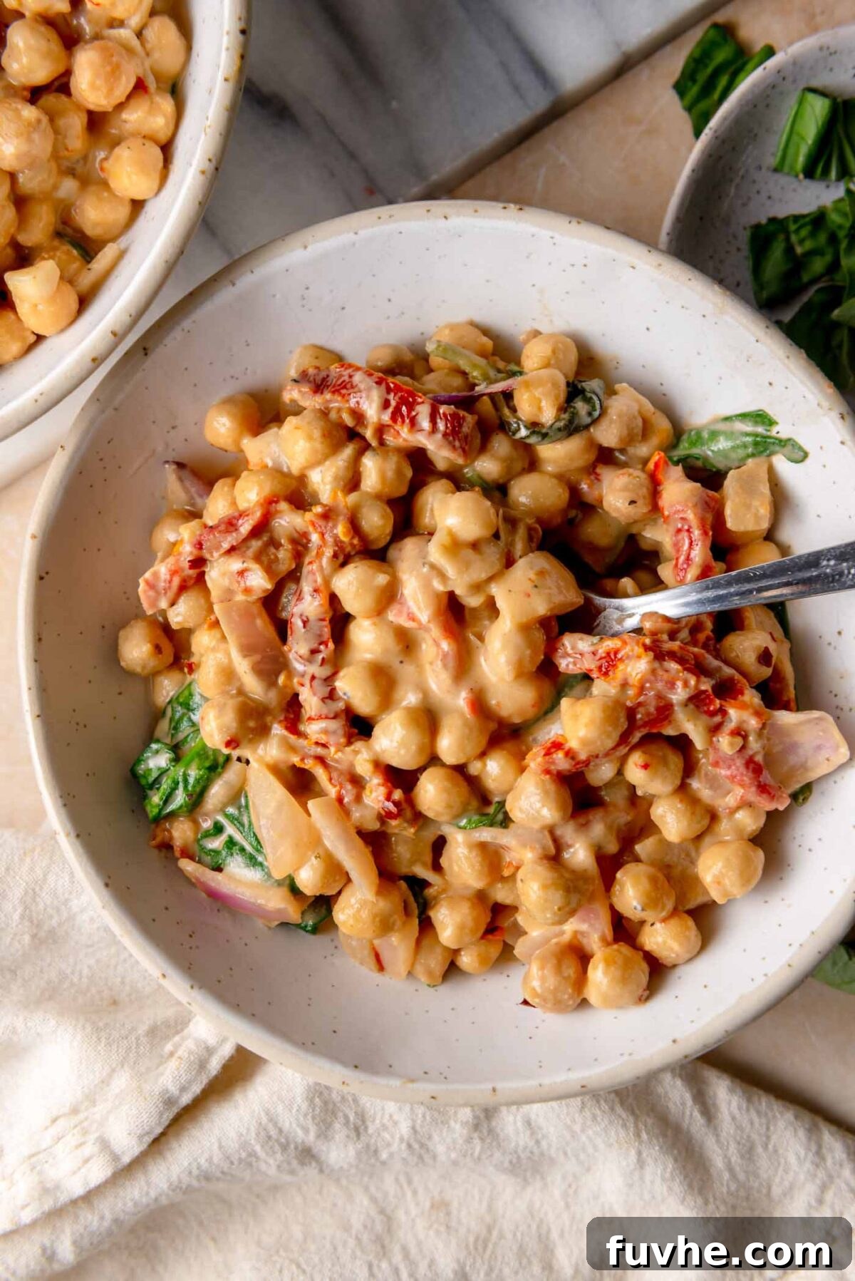 Head Over Heels for Chickpeas 9 White bowl filled with creamy 'Marry Me' chickpeas, coated in a rich cashew-based sauce with sun-dried tomatoes and spinach, ready to serve.