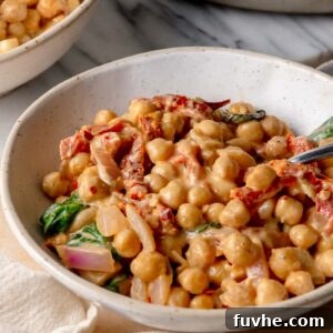 Creamy 'Marry Me' chickpeas with sun-dried tomatoes and spinach served in a white bowl with a spoon.