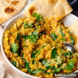 Bowl of spinach red lentil curry served with piece of naan and fresh cilantro on top.
