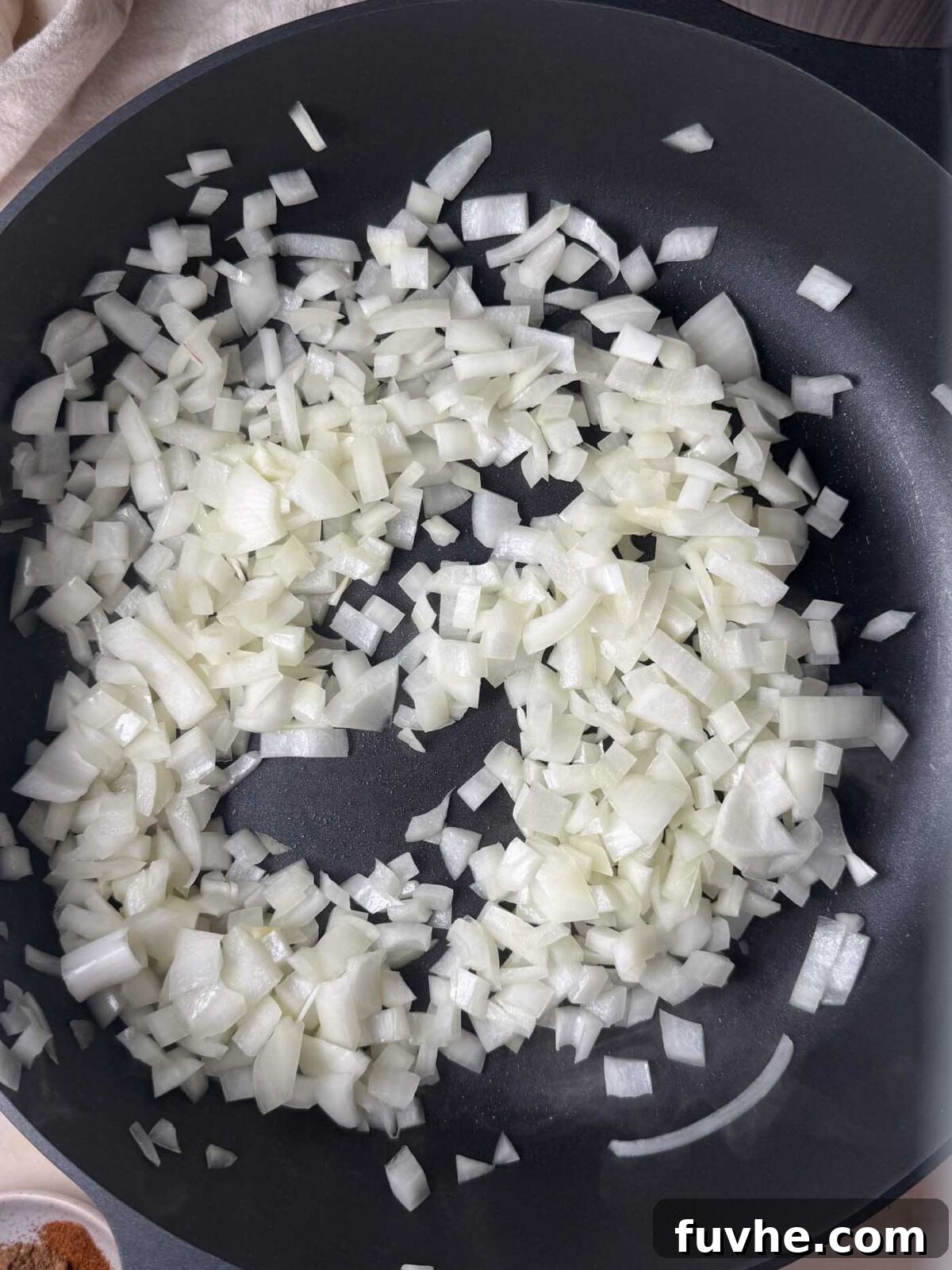 Chopped white onion sautéing in a large nonstick pan before.
