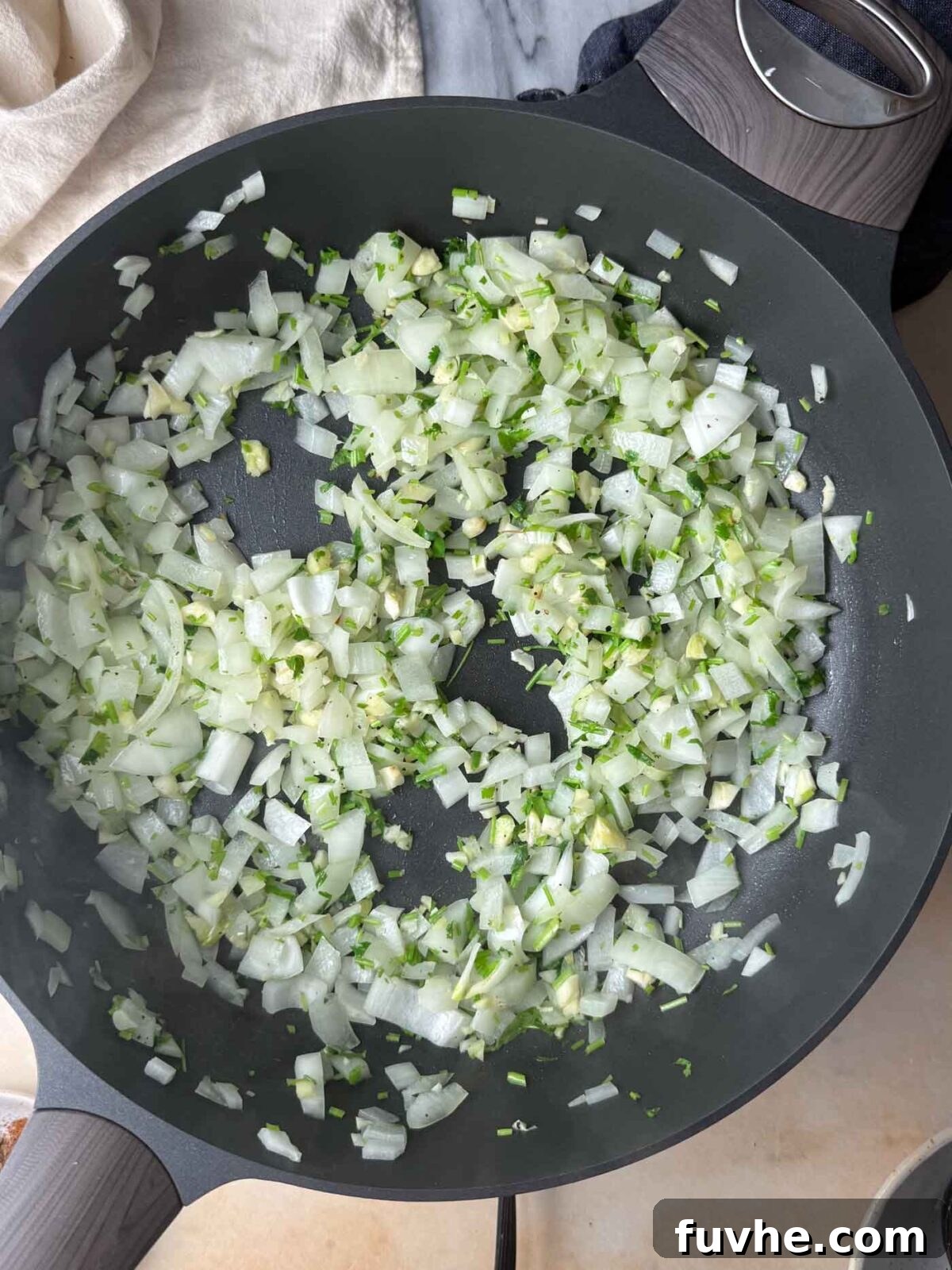 Diced onion cooking with garlic and fresh herbs in a skillet.