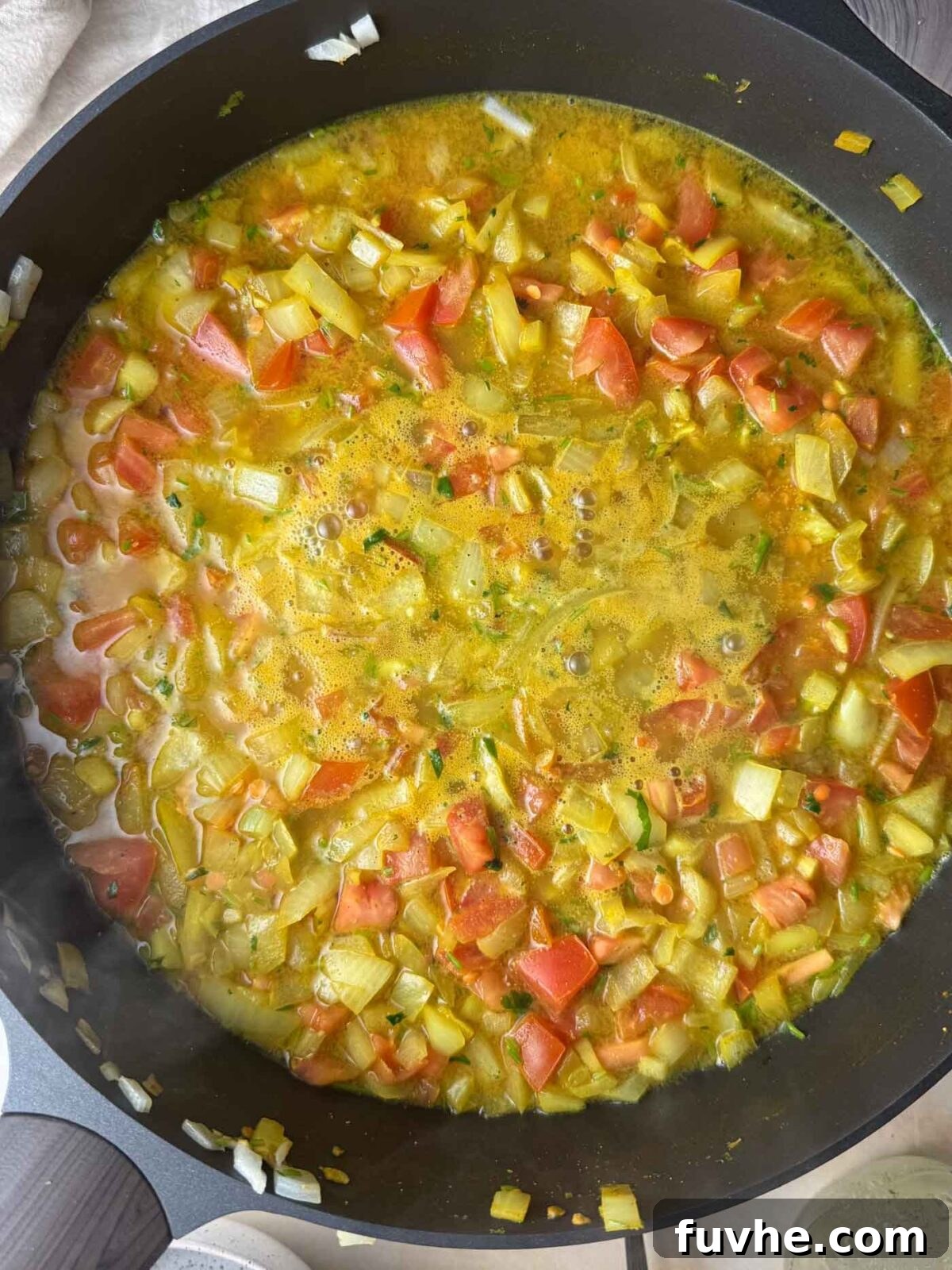 Onion and tomato mixture covered with golden-colored liquid in a pan.