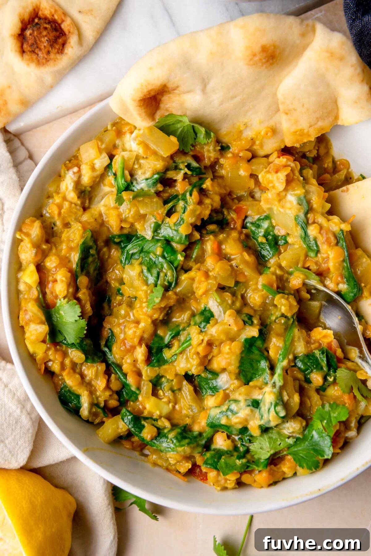 Overhead view of a bowl of spinach and red lentil curry with naan bread.