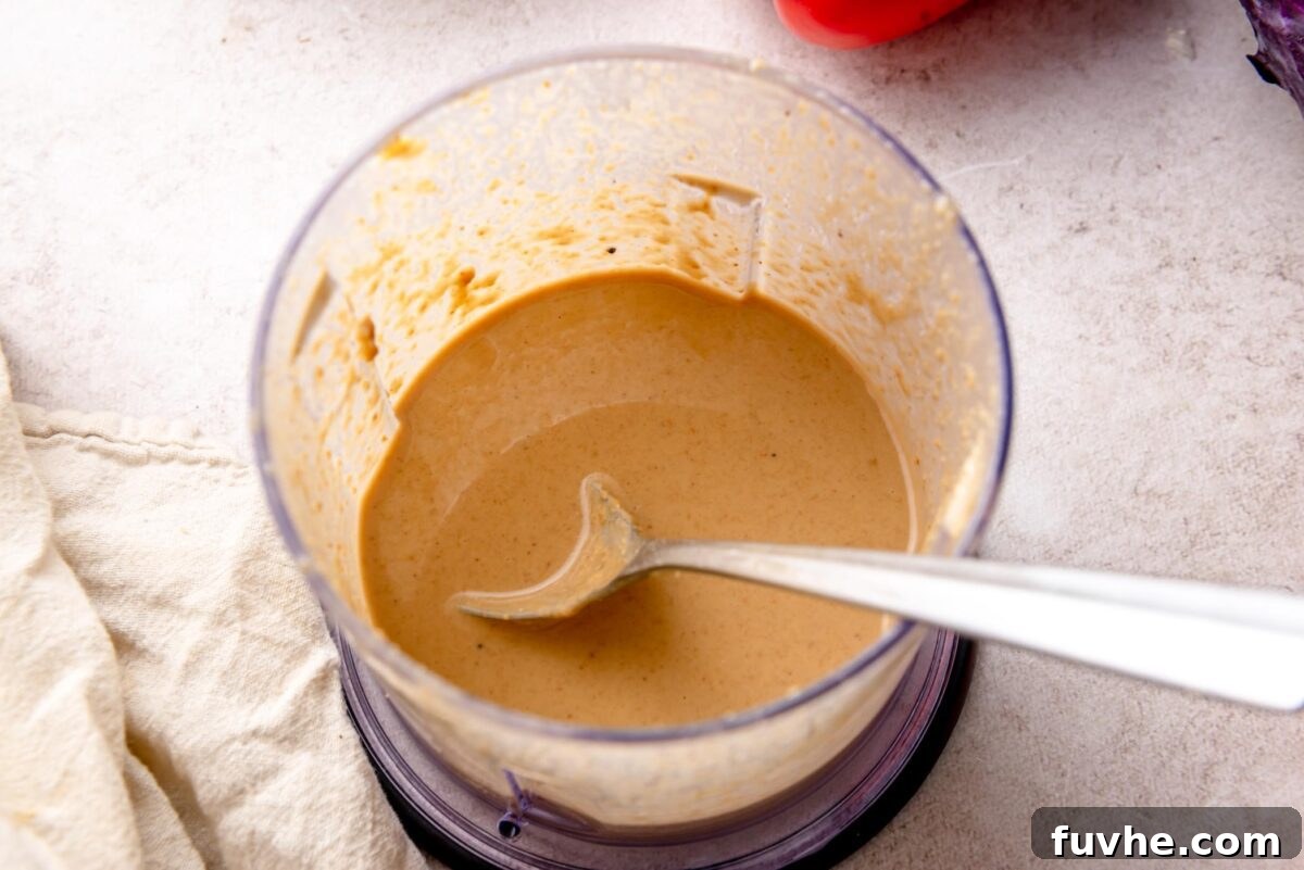 Peanut sauce blended in a food processor until smooth and creamy, with a spoon showing the thick, pourable texture.