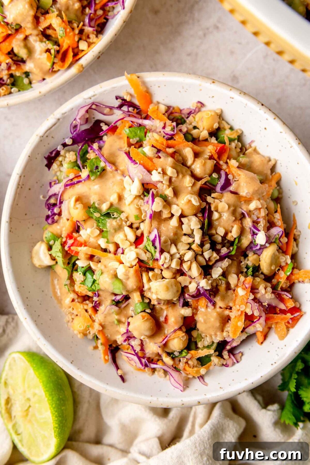 Thai peanut quinoa salad served in a bowl, topped with chopped peanuts and cashews and finished with a squeeze of fresh lime.