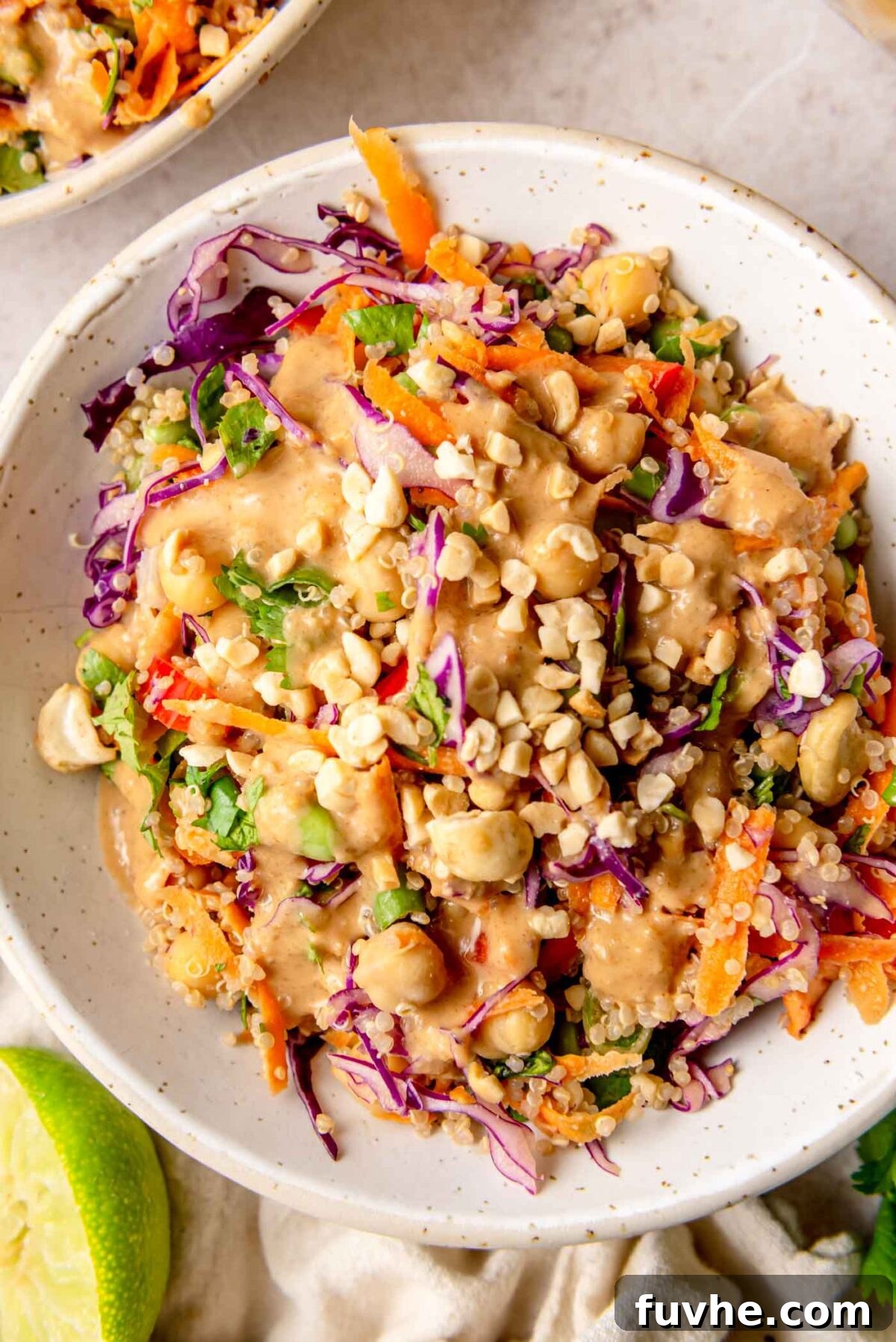 Thai peanut quinoa salad served in a bowl, topped with chopped peanuts and cashews and finished with a squeeze of fresh lime.