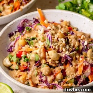 Detailed close-up of quinoa salad with red cabbage, carrots, edamame, chickpeas, herbs, and peanut sauce coating everything.
