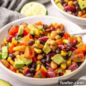 Three bean chipotle salad with corn, bell peppers, and avocado served in a white bowl with lime.