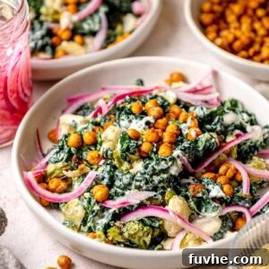 Roasted vegetable Caesar salad with crispy chickpeas, kale, broccoli, cauliflower, and pickled red onions in a creamy dressing, served in a shallow bowl.