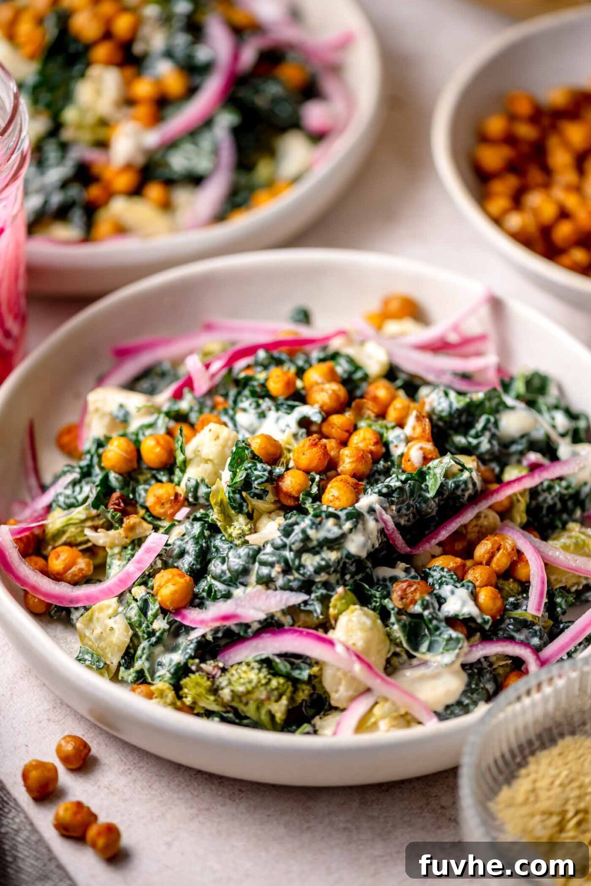 Golden Roasted Vegetable Caesar 10 Finished roasted vegetable Caesar salad with crispy chickpeas, kale, broccoli, cauliflower, and pickled red onions in a creamy dressing, served in a shallow bowl and ready to eat.
