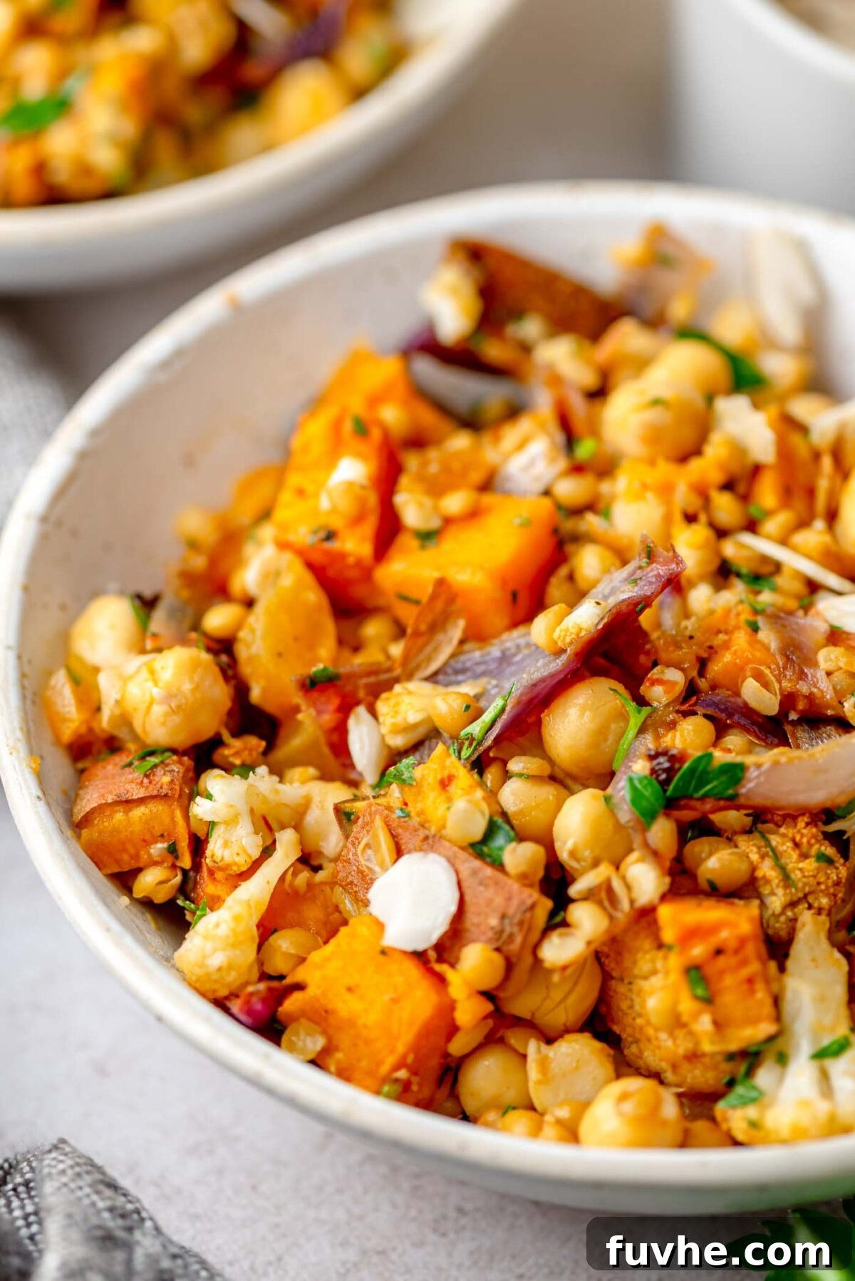 A vibrant bowl of Harissa Roasted Vegetable Lentil Salad, showcasing caramelized sweet potato, cauliflower, chickpeas, and fresh herbs.