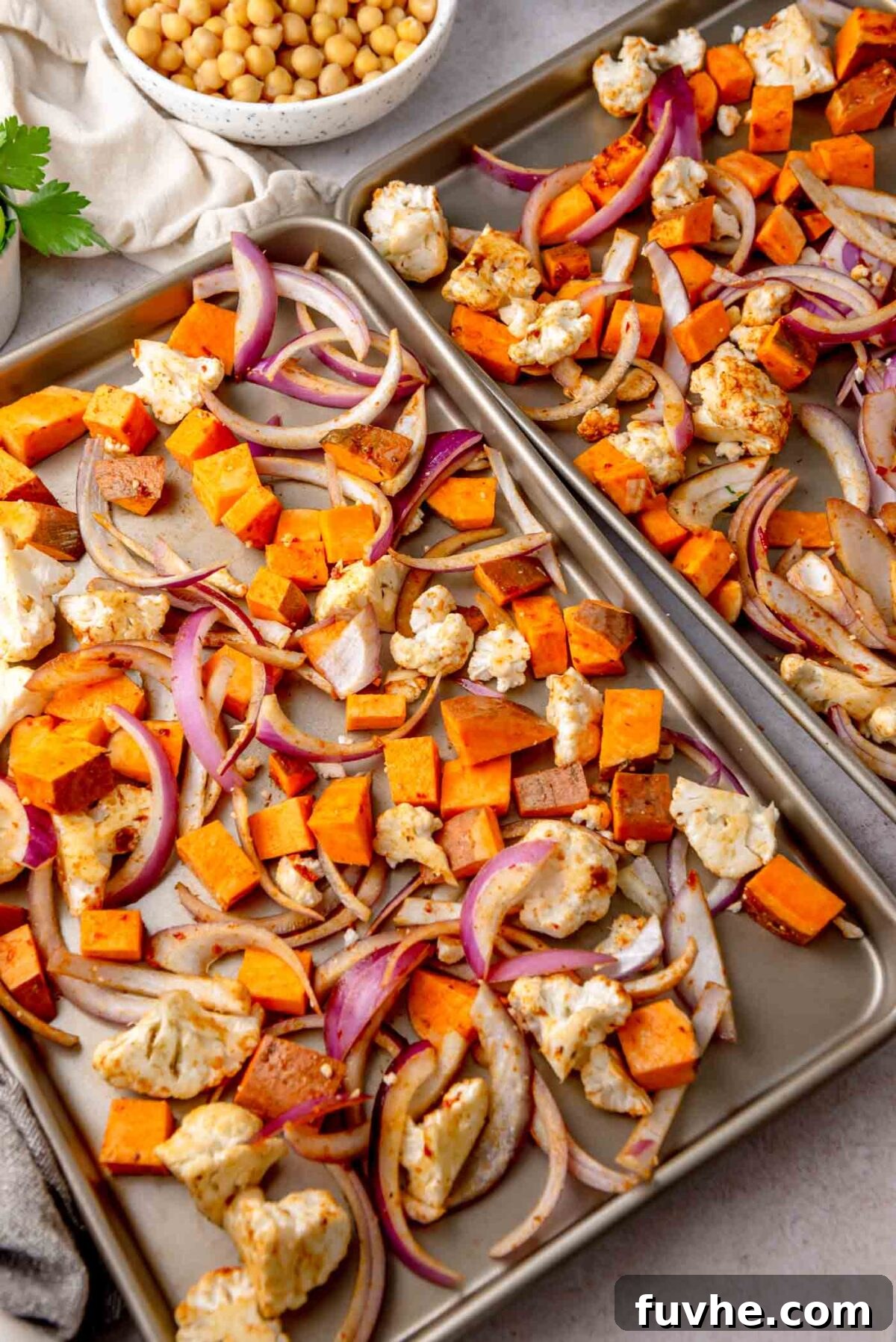 Seasoned vegetables spread out on two baking sheets, ready for the oven.