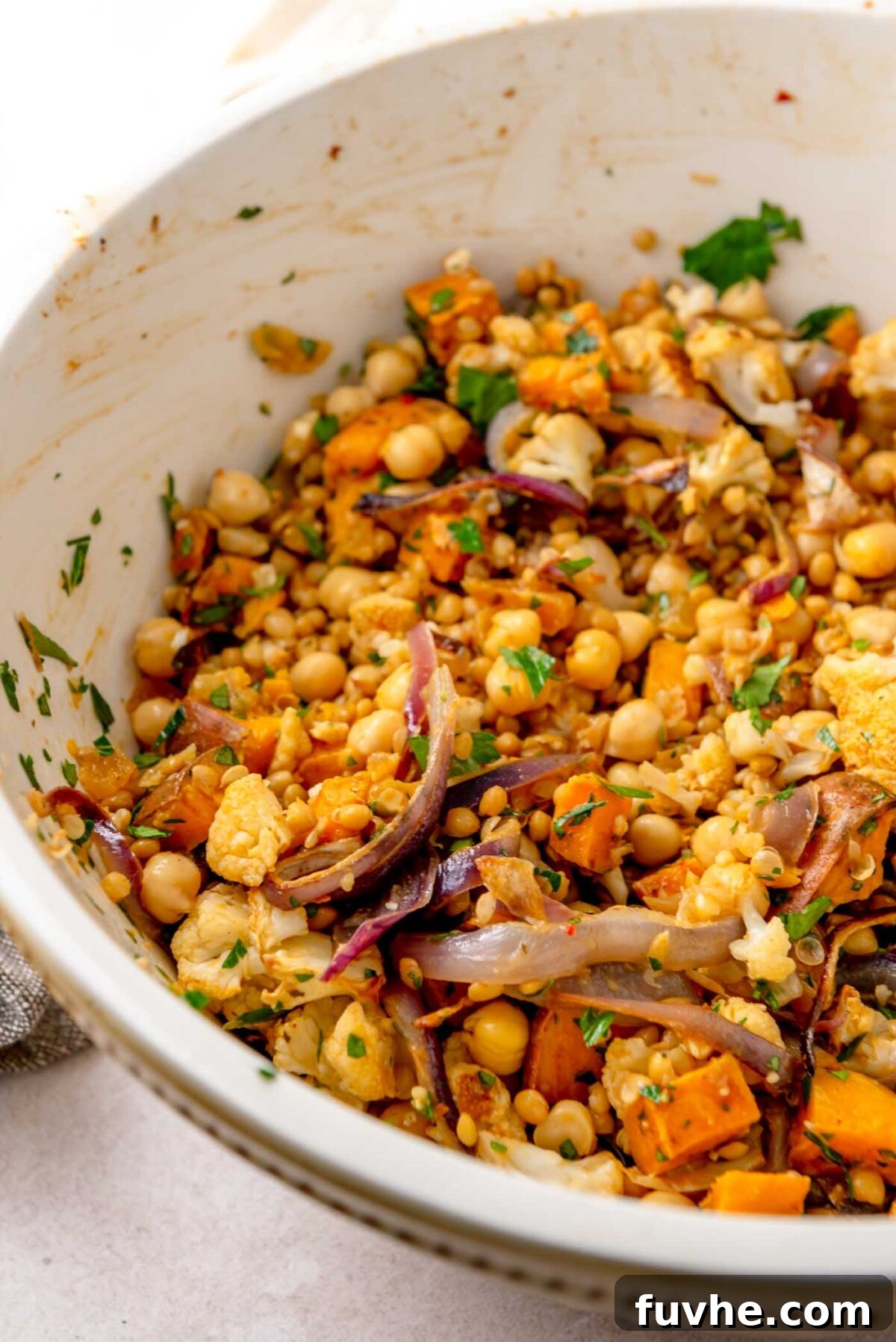 Roasted vegetables, lentils, chickpeas, and herbs being tossed with the dressing in a large bowl.